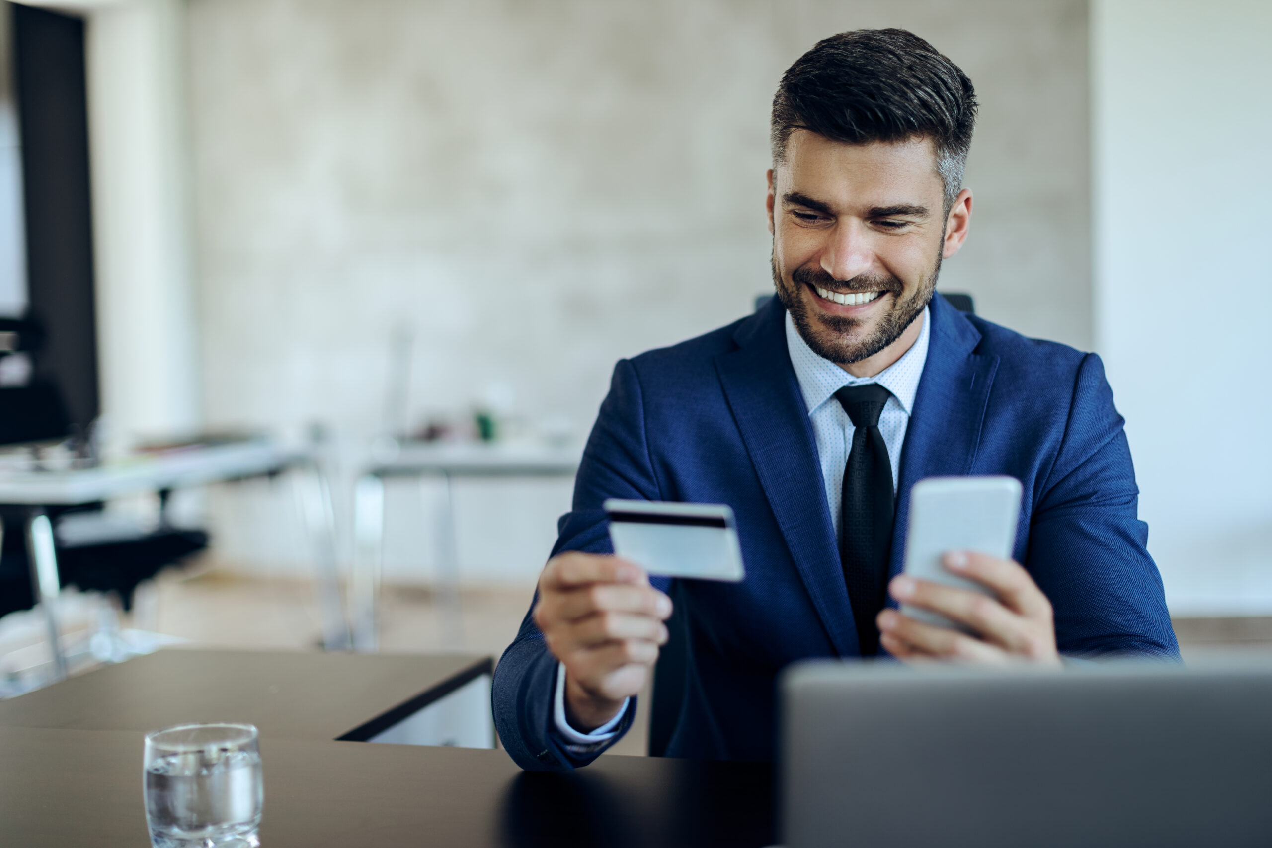 Happy businessman using smart phone and credit card for online shopping while working in the office.